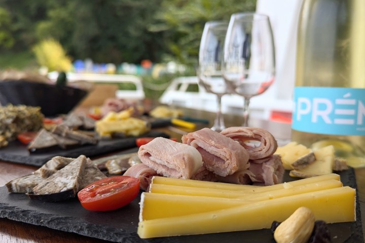 Charcuterie board with meats, cheese, tomato; wine bottle and glasses in background.