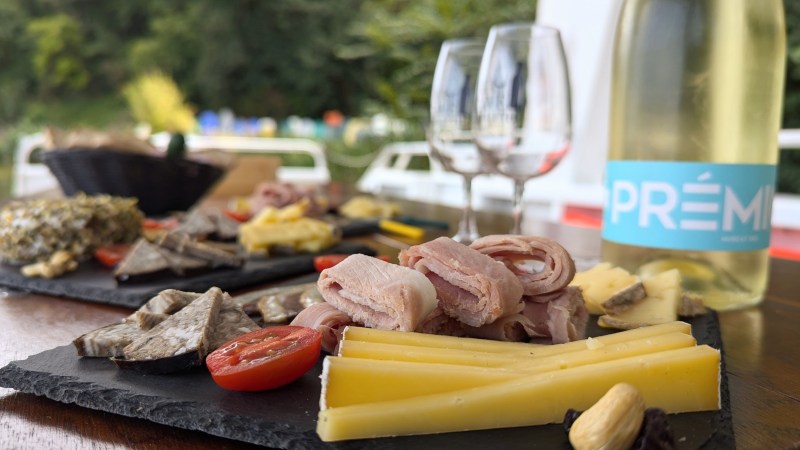 Charcuterie board with meats, cheese, tomato; wine bottle and glasses in background.