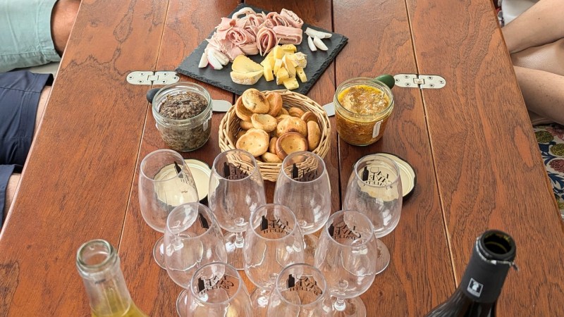 People seated around a table with snacks, wine glasses, and bottled drinks.