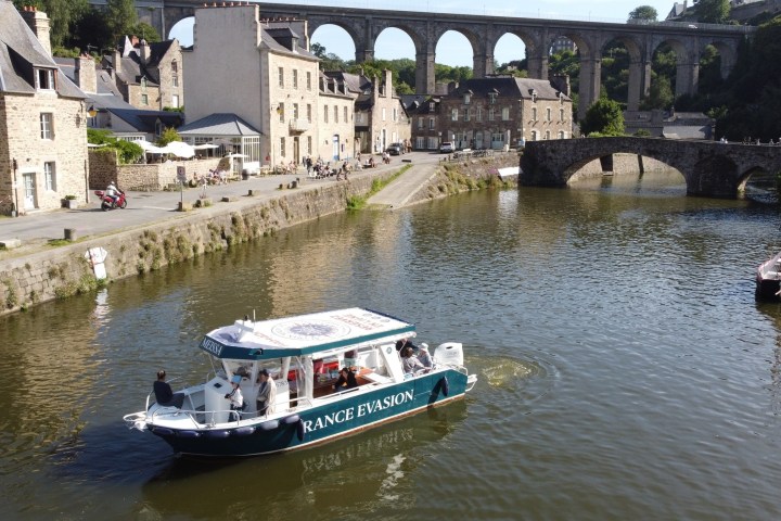 Boat on a river by stone buildings and arched bridge in a quaint village.