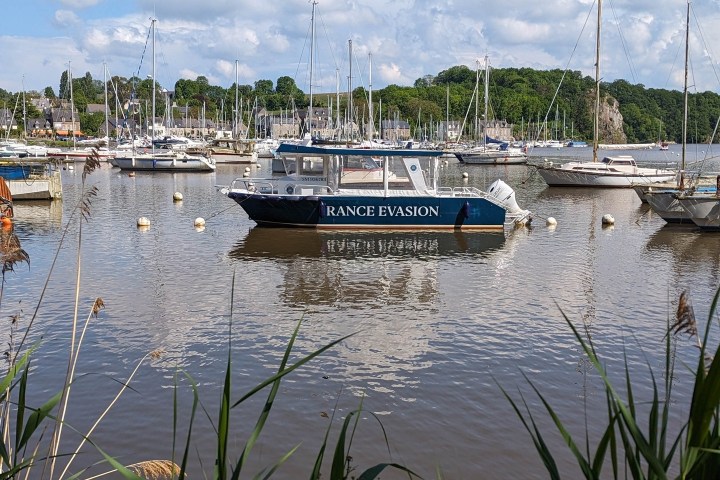 Boat named 'Rance Evasion' in a calm marina surrounded by reeds and sailboats.