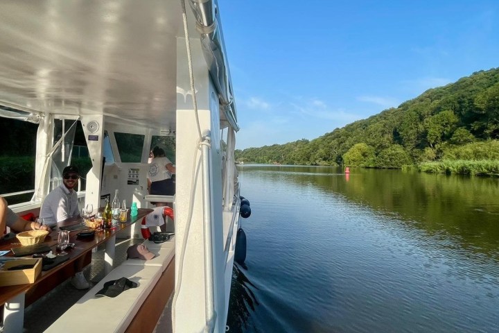 People on a boat cruising a calm river with trees on the riverbank.