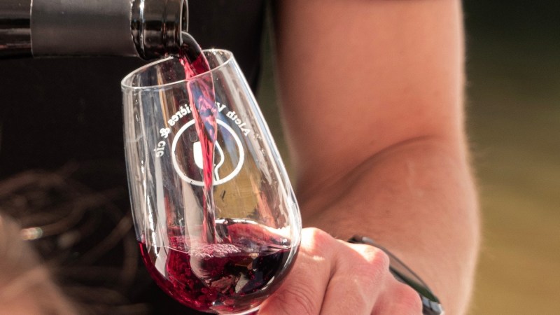 Red wine being poured into a clear wine glass held by a person.