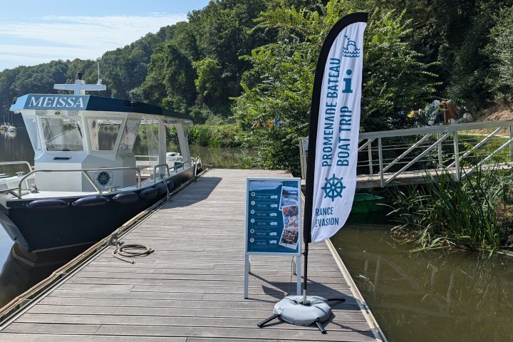 Boat moored at a wooden dock with boat trip sign and trees in background.