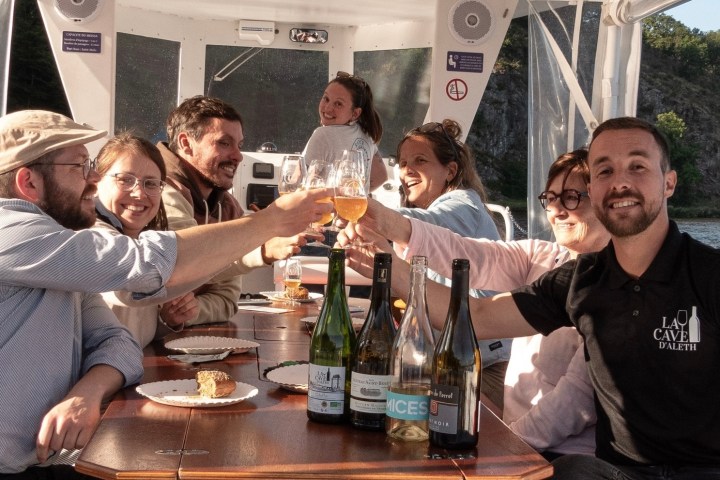 Group toasting drinks on a boat with wine bottles on the table.