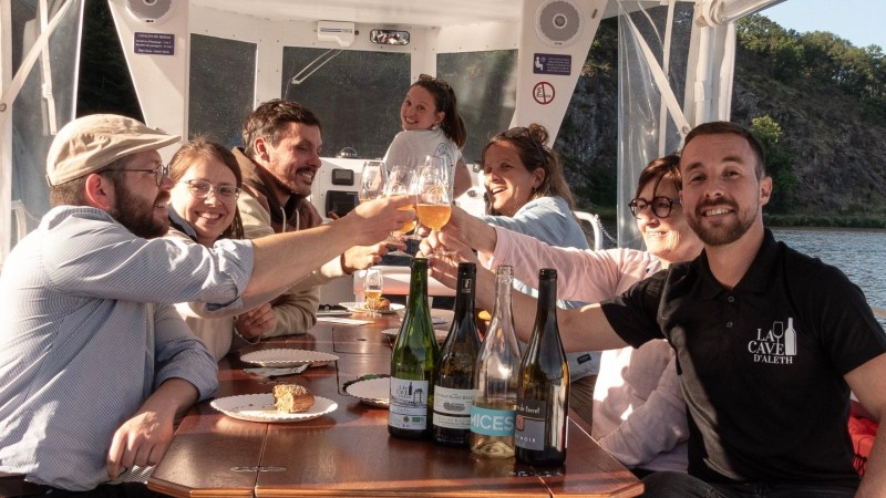Group toasting drinks on a boat with wine bottles on the table.