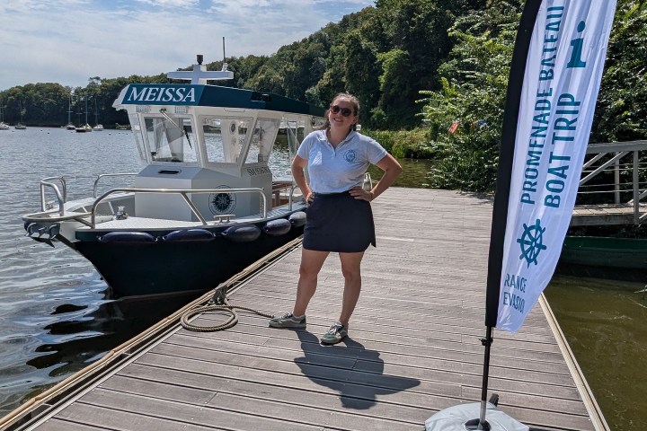 Person on a dock beside a boat and flag under a blue sky.