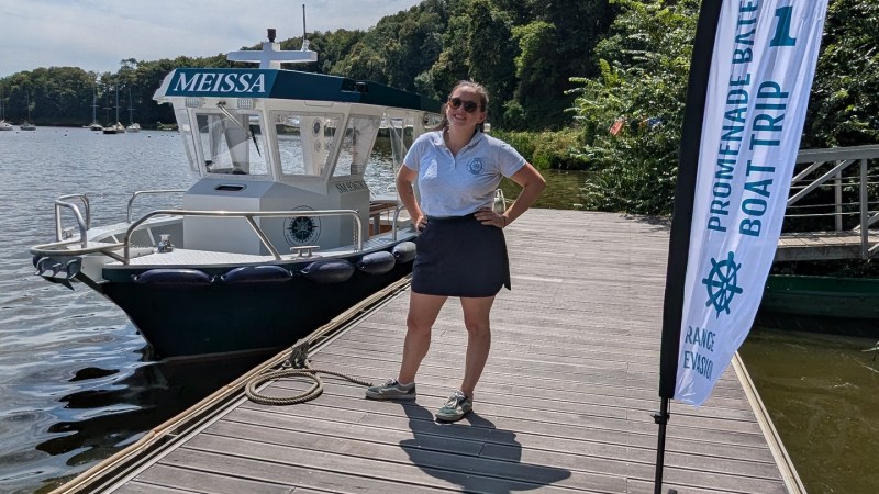 Person on a dock beside a boat and flag under a blue sky.