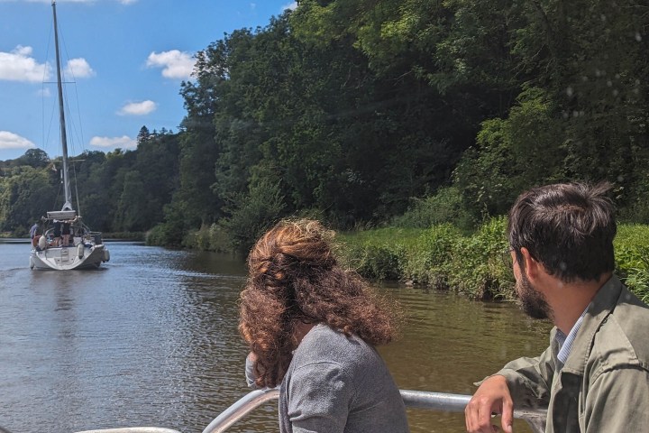 Two people on a boat observing another boat on a calm river.