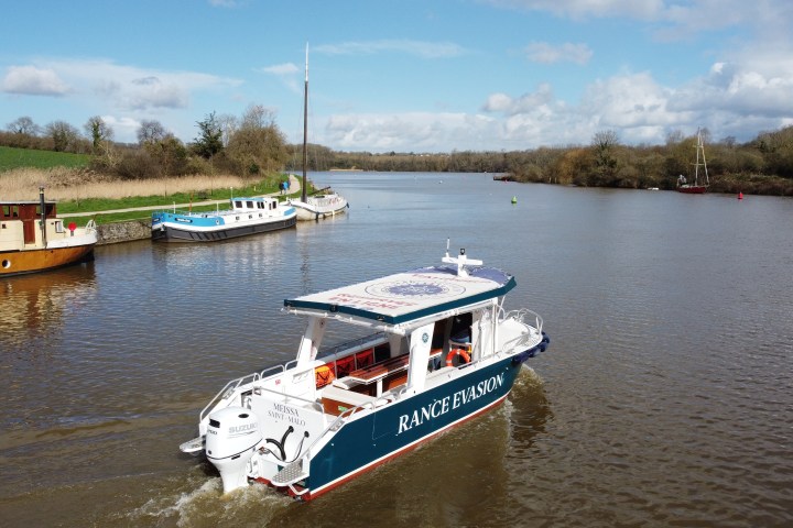 Small passenger boat on a river with trees and a cloudy sky.
