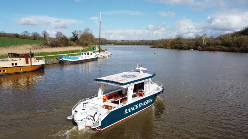 Small passenger boat on a river with trees and a cloudy sky.
