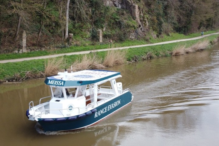 Small boat named 'MEISSA' on a river near a wooded path.