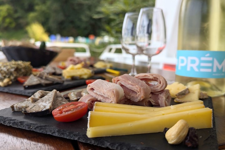 Cheese and charcuterie with wine and empty glasses on a table outdoors.